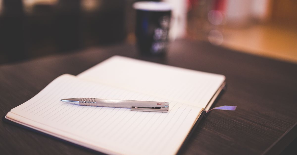 An open lined notebook with a silver pen laying on a dark wooden table.