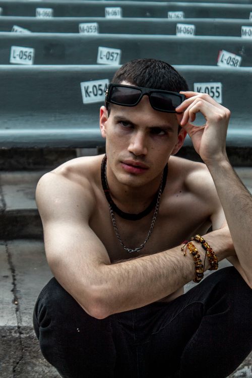 Free A young man sitting on stadium steps, wearing sunglasses and accessories, exuding a confident vibe. Stock Photo