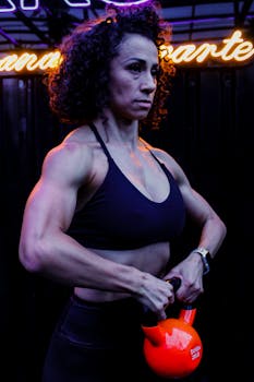 Focused female athlete working out with a kettlebell in an indoor gym setting.