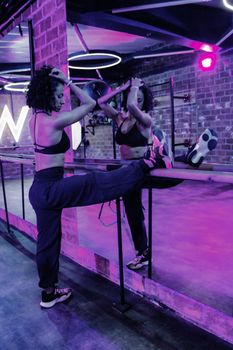A woman stretches her leg on a barre in a dance studio with vivid purple lighting.
