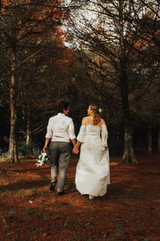 A couple holding hands, walking in a forest, captured from behind, emphasizing natural beauty and love.