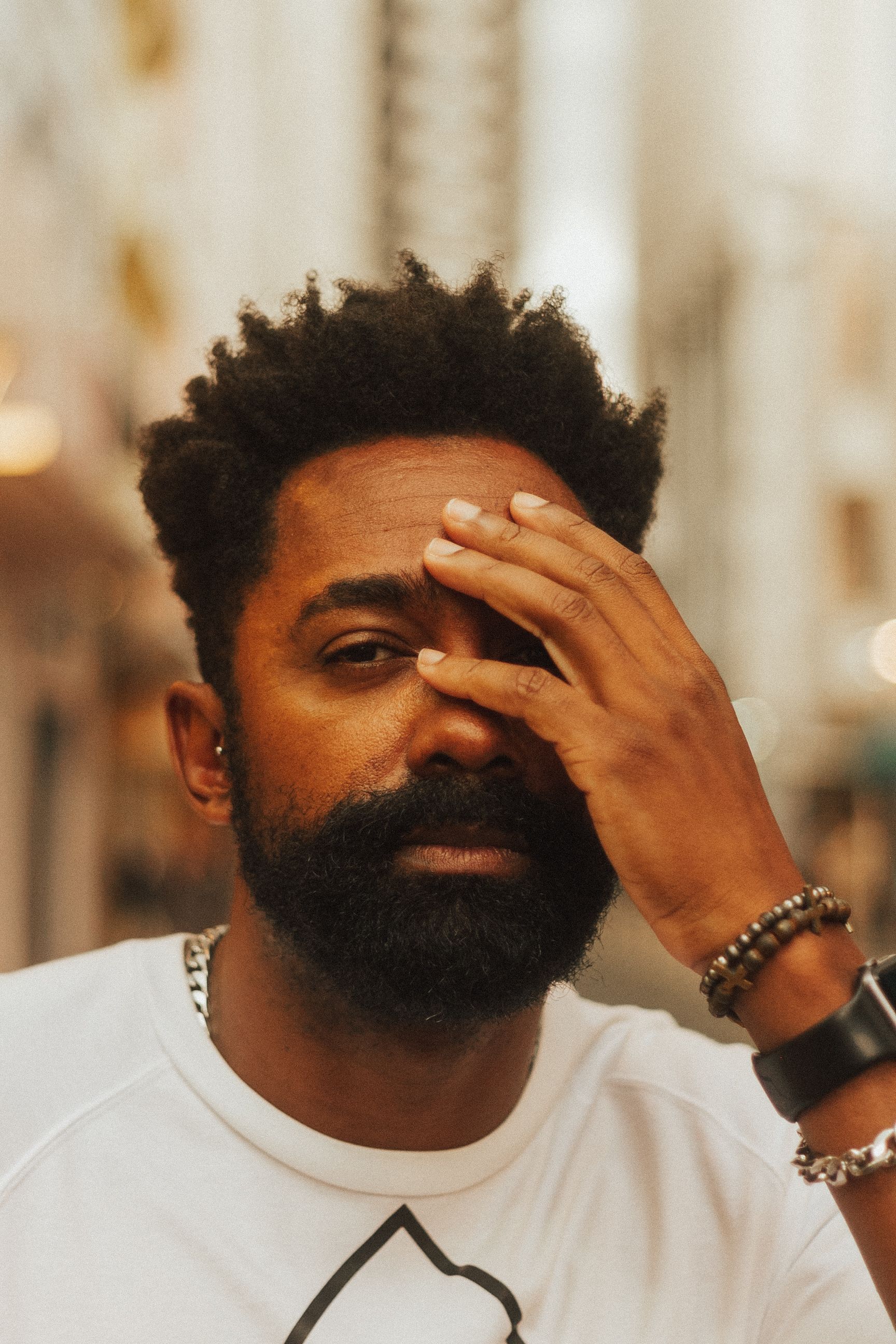 Portrait of a bearded man outdoors, partially covering his face with his hand, in a city setting.