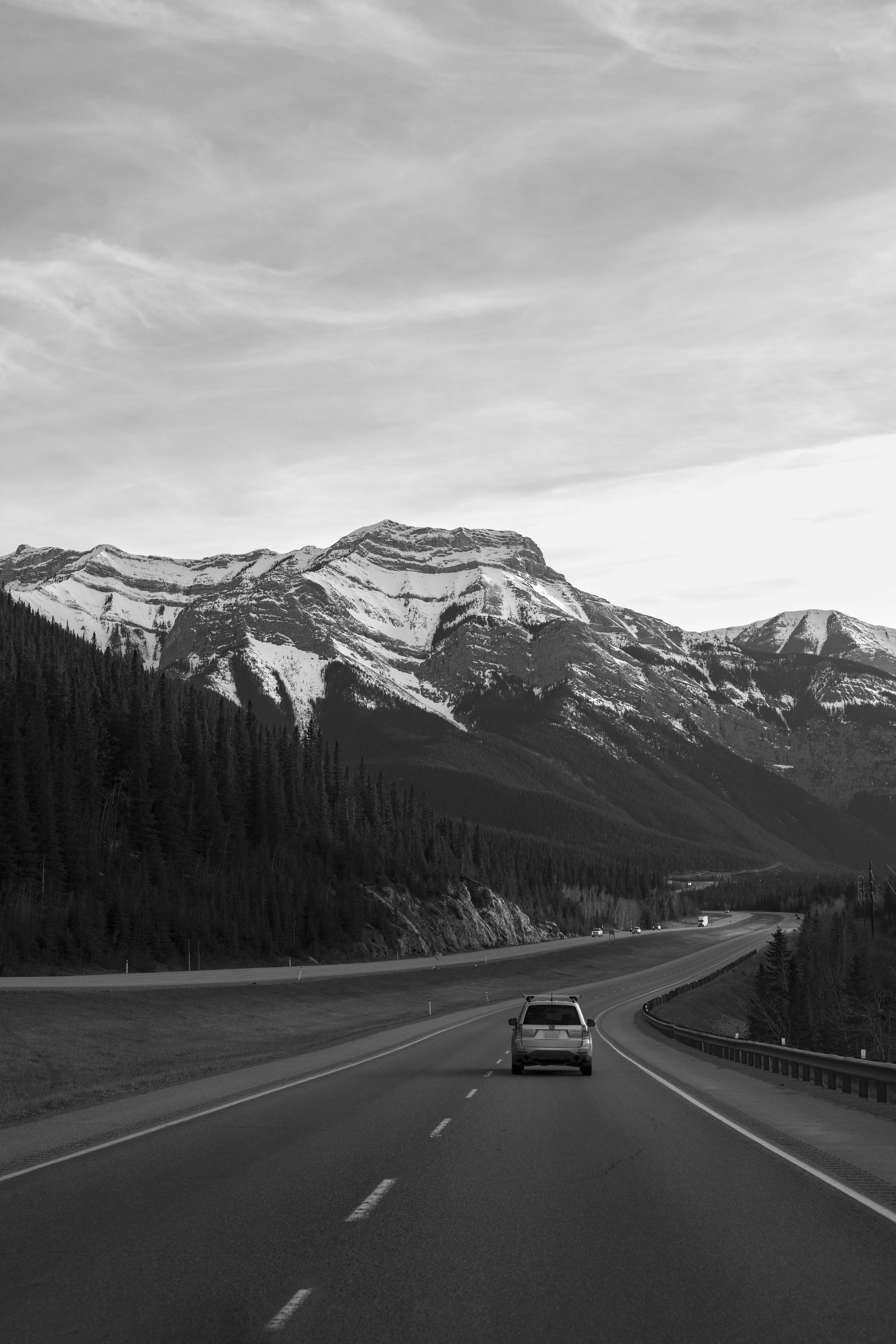 Black and white shot of a car traveling through snowcapped mountains in Banff, Canada. Scenic and serene.