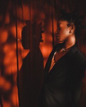 Stylish woman in a black suit posing dramatically with artistic red shadow backdrop.