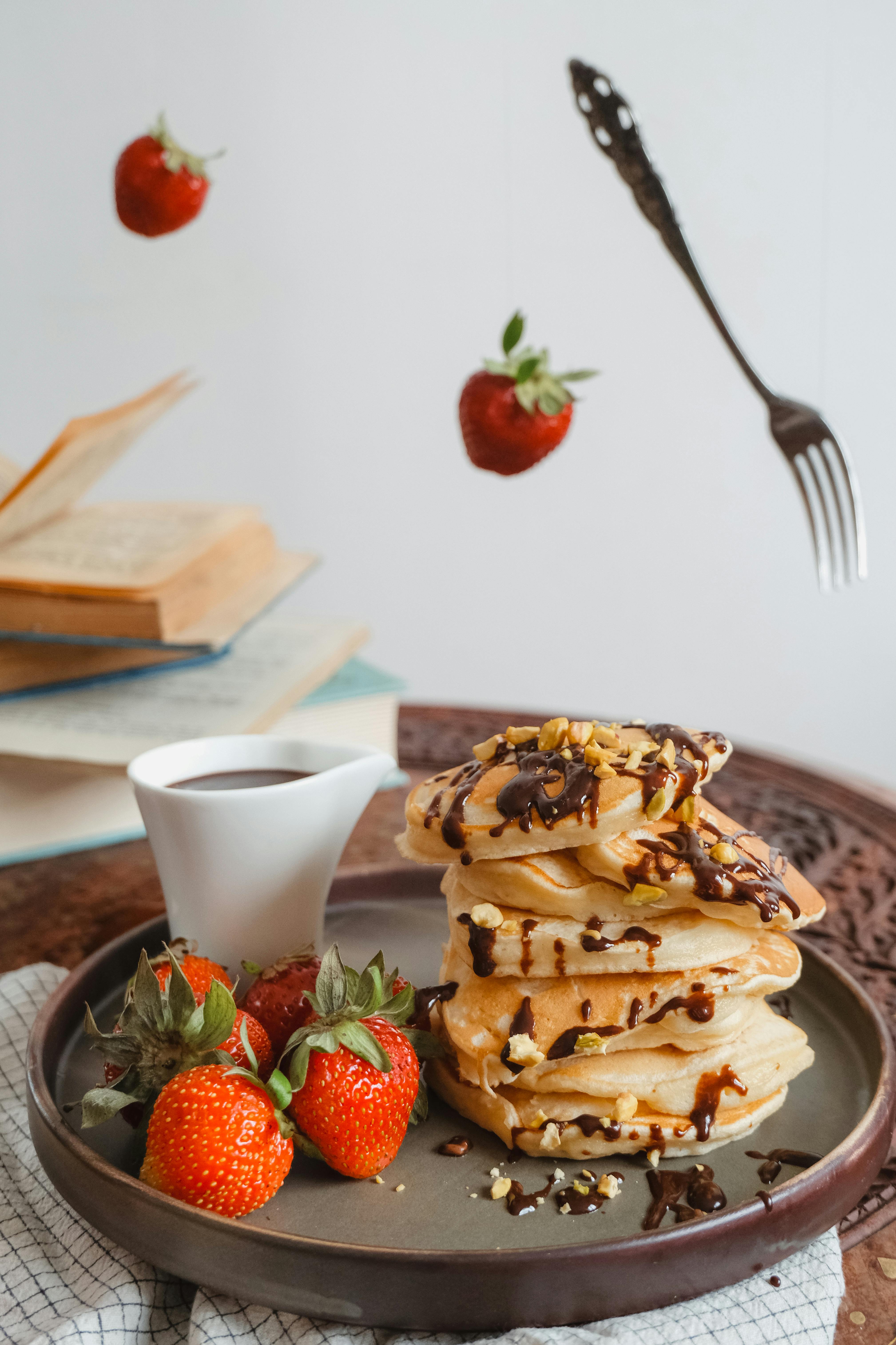 flying fork and strawberries around plate with pancakes and cup