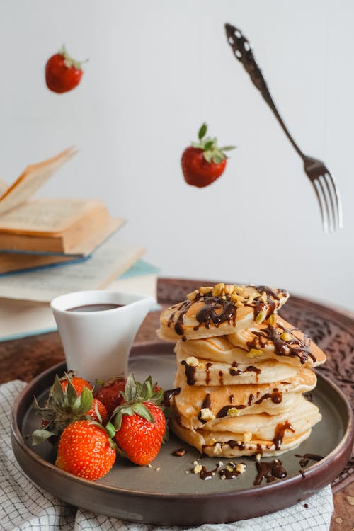 Free Flying Fork and Strawberries around Plate with Pancakes and Cup Stock Photo