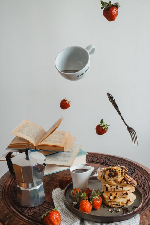 Free A surreal breakfast setting with floating strawberries, pancakes, and books. Stock Photo
