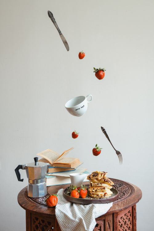 Free Unique artistic composition of pancakes and strawberries floating above a table. Stock Photo