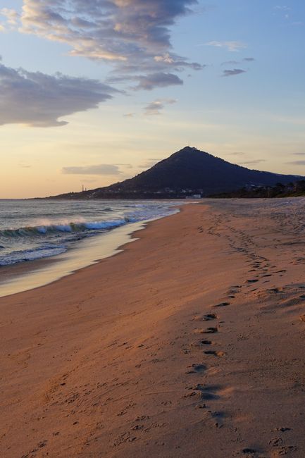 Golden sunset over a tranquil beach with mountain backdrop, perfect for travel and relaxation themes.