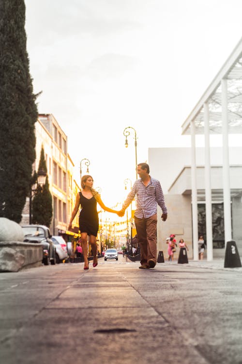 Free Man and Woman Walking on Street While Holding Hands Stock Photo