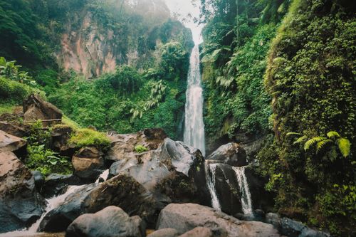 Free A breathtaking view of a waterfall cascading through rocky terrain surrounded by lush greenery. Stock Photo