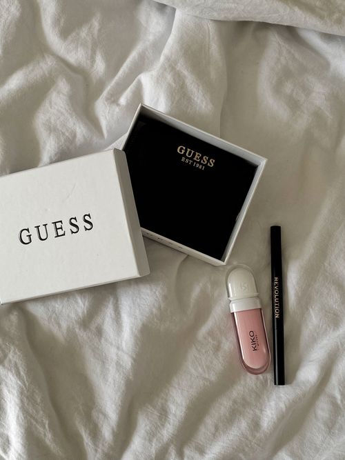Free Top view of Guess accessories box with makeup essentials on white fabric. Chic and modern aesthetic. Stock Photo