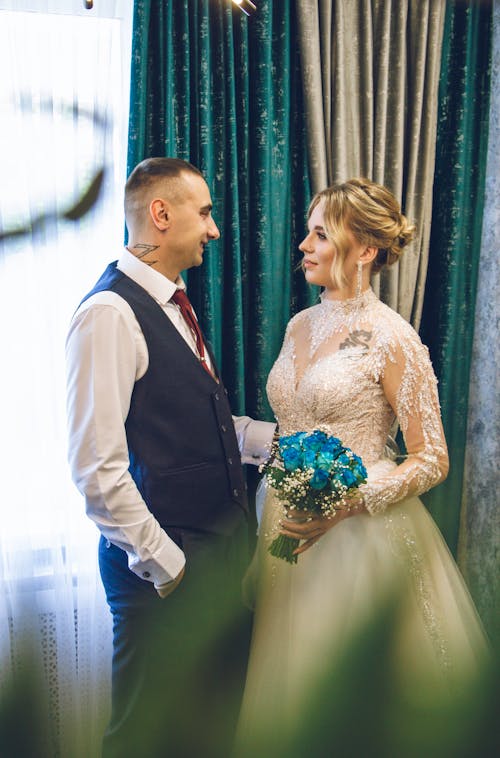 Newlyweds Standing near Curtains and Posing