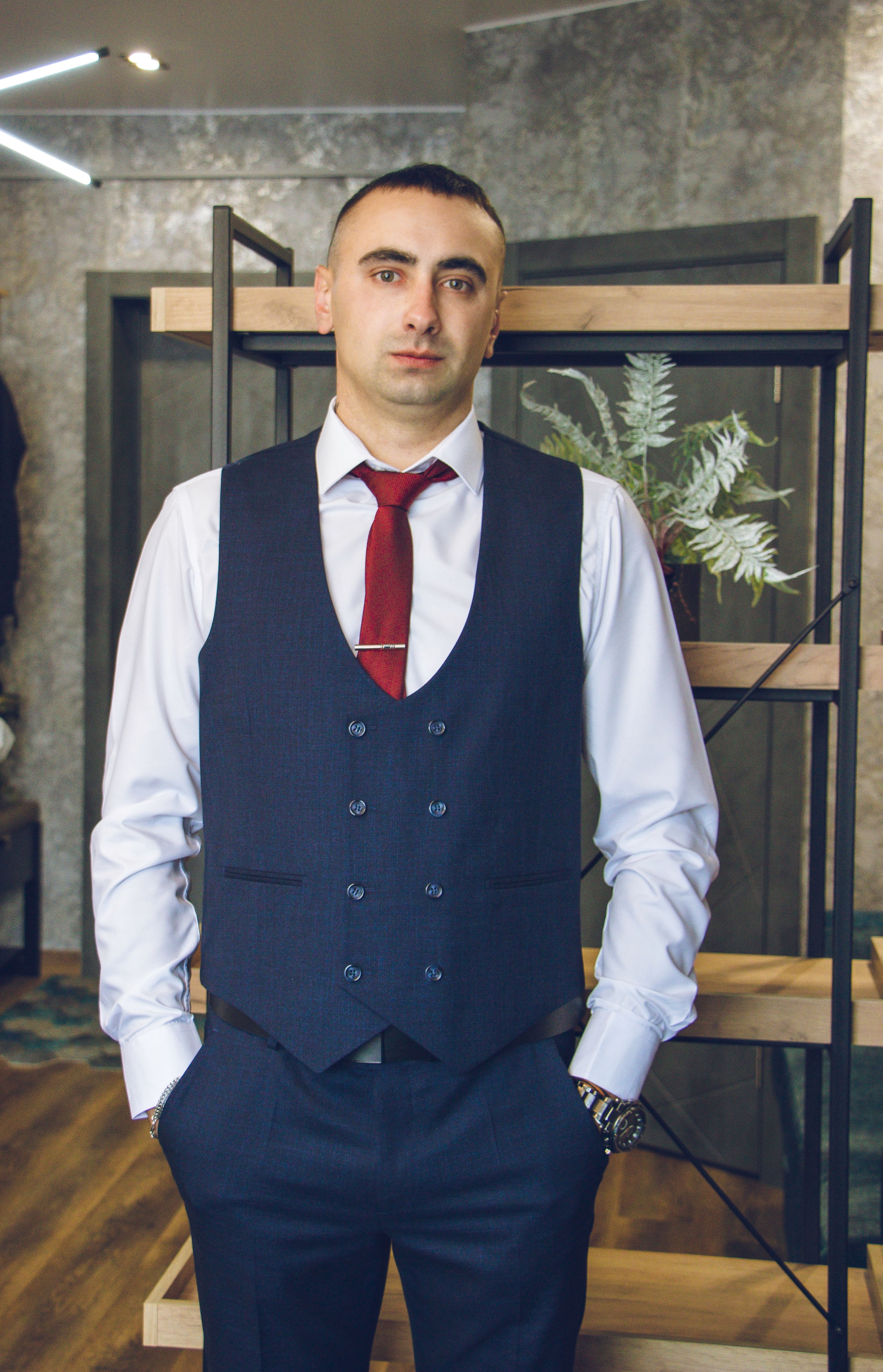 Portrait of a stylish man in a vest and tie, standing confidently in a modern indoor setting.