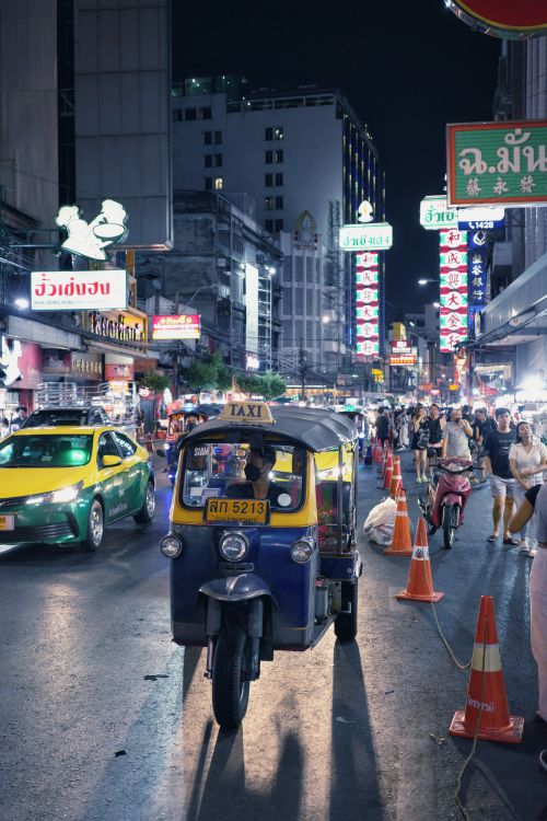 Free A vibrant street in Bangkok at night with a tuk tuk and neon lights capturing urban life. Stock Photo