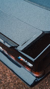 Close-up of a sleek black car trunk with rain droplets enhancing its design.