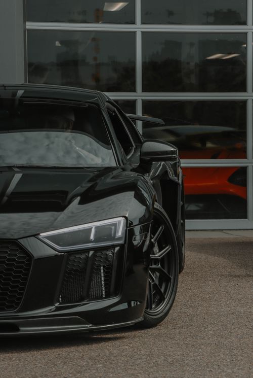 Free Dynamic view of a sleek black supercar parked indoors with a reflective glass backdrop. Stock Photo
