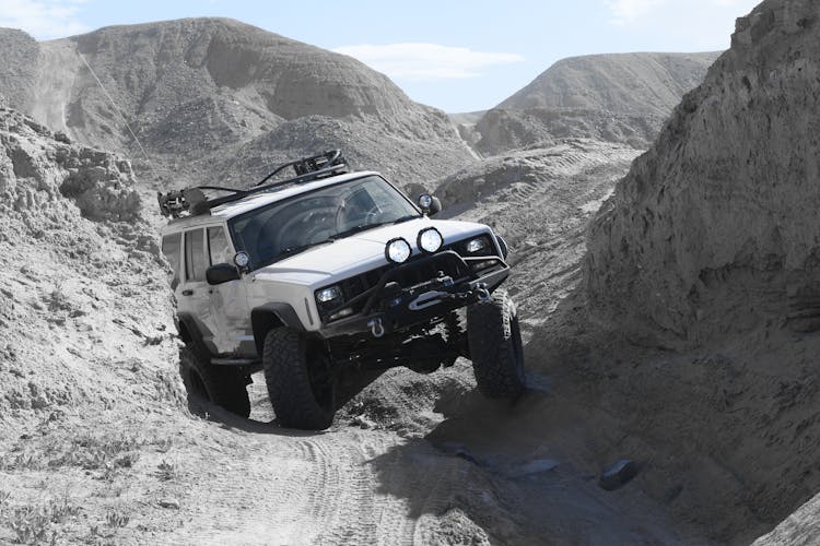 White Jeep Cherokee With Suspension Lift Crossing Rough Rocky Terrain