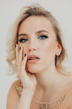 Portrait of a thoughtful blonde woman with hand on cheek against a white backdrop, highlighting elegance and introspection.