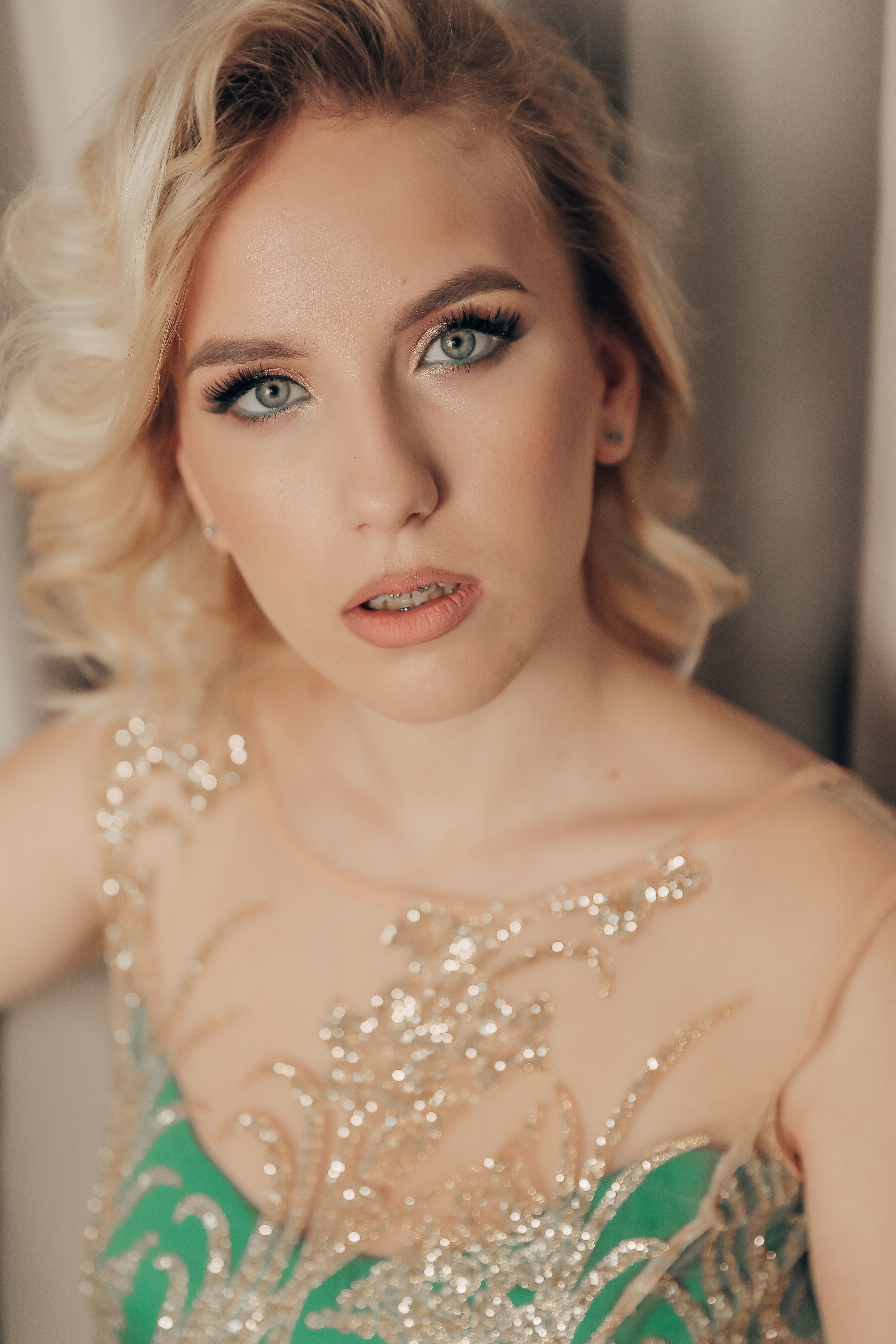Glamorous portrait of a young blonde woman in a green beaded dress, exuding elegance.