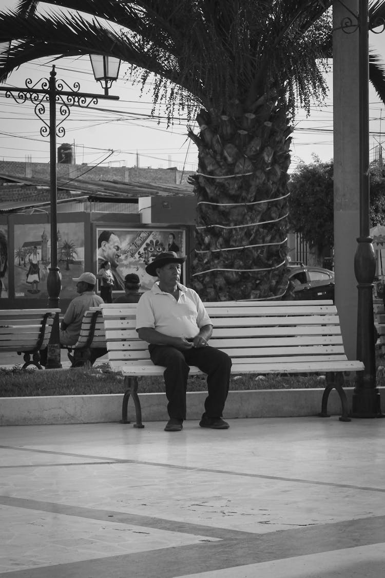 Black And White Photo Of A Man In Cowboy Hat Sitting On A Bench