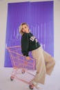 Blonde Woman in Sweatshirt Posing on Pink Shopping Cart in Studio