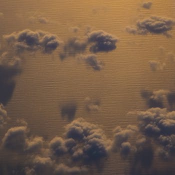 Dramatic aerial image of clouds casting shadows over a golden ocean at sunset, creating a serene and abstract seascape.