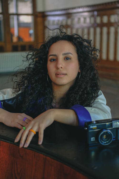 A woman with curly hair sitting at a table with a camera