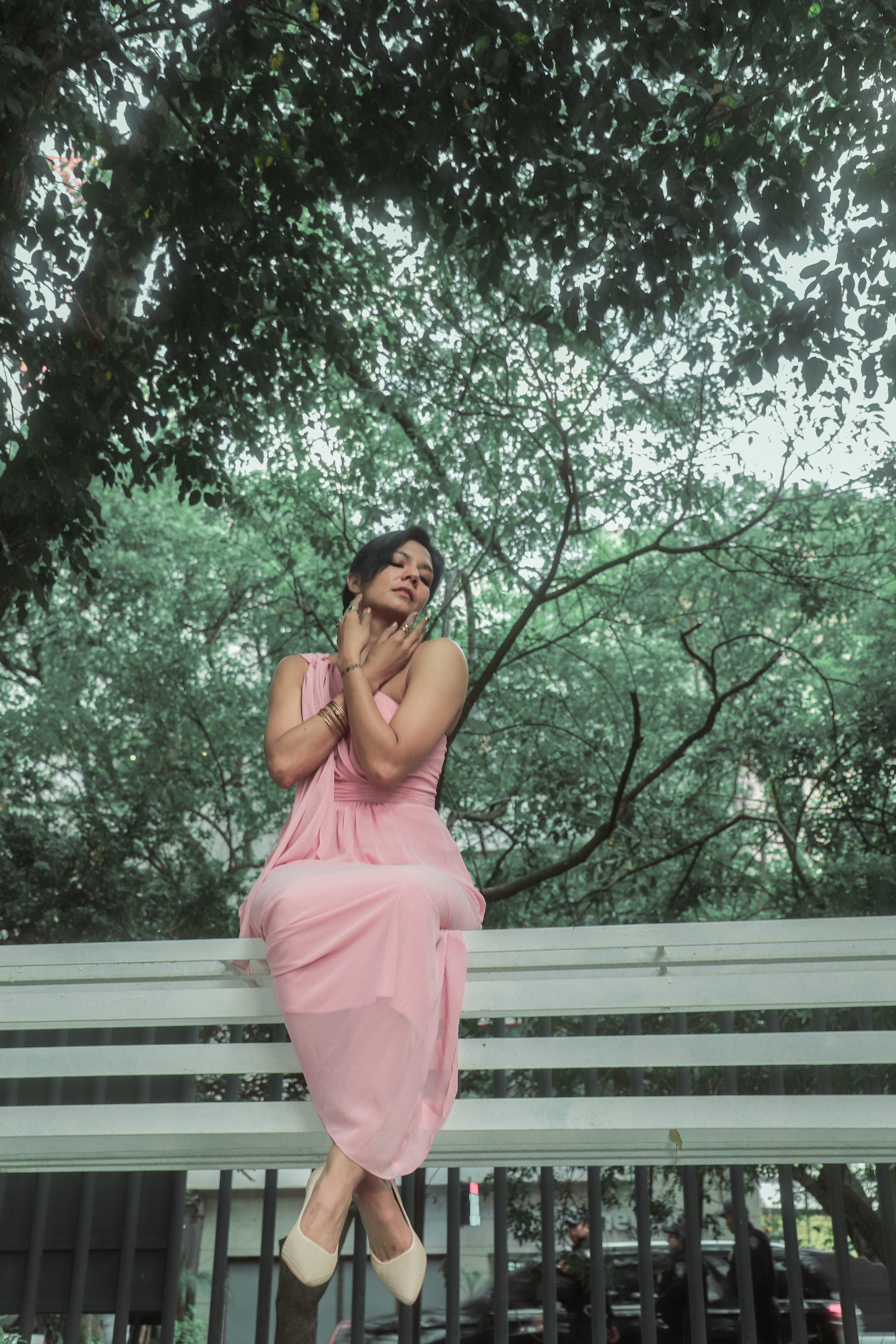 Fotomural Una mujer posando elegantemente en un vestido rosa en un banco en un entorno exuberante de parque en Ciudad de México.
