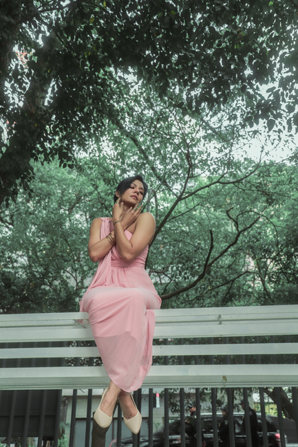 Fotomural Una mujer posando elegantemente en un vestido rosa en un banco en un entorno exuberante de parque en Ciudad de México.