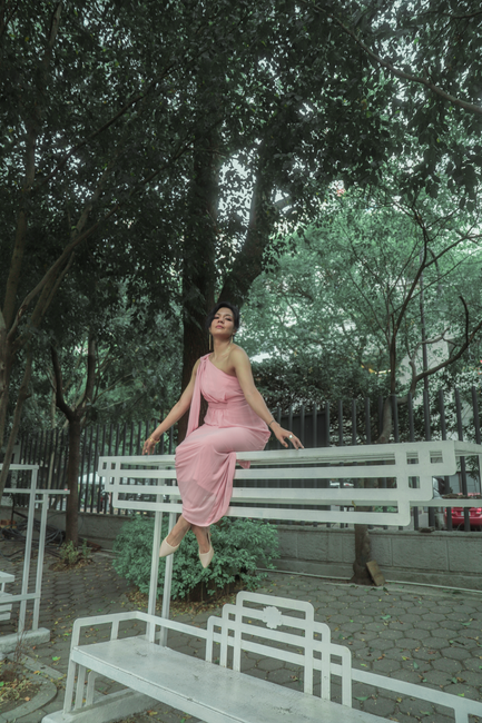Fotomural Una mujer con un vestido rosa posa elegantemente en un banco en un frondoso parque urbano en la Ciudad de México.