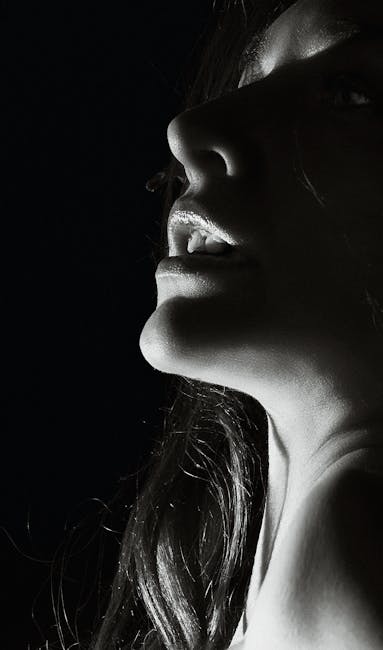 Artistic black and white portrait of a woman's face in low key lighting, highlighting dramatic features.