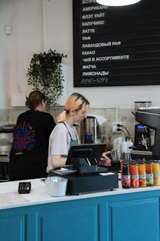Two baristas working at a coffee counter in a modern café setting, preparing beverages.