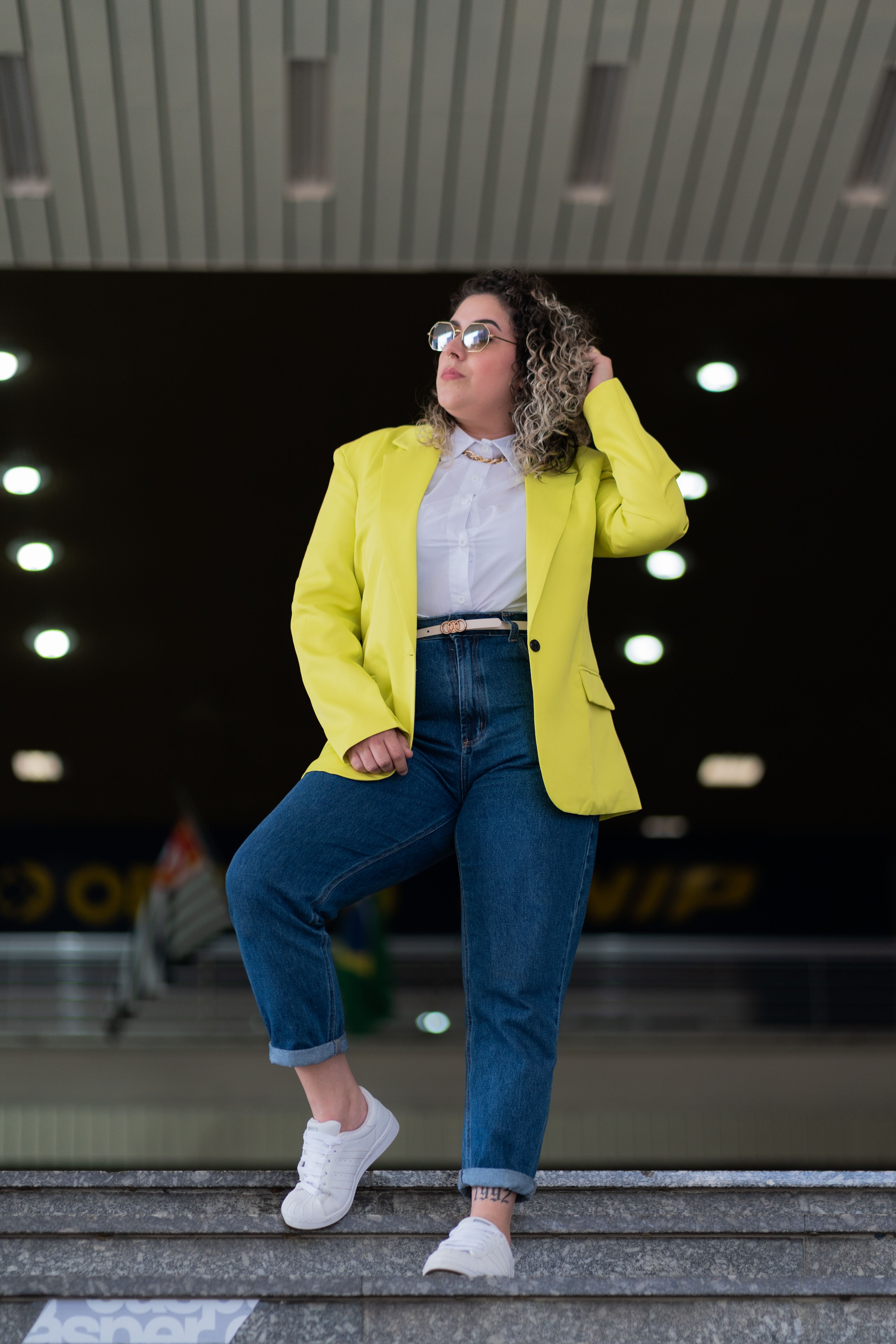 Mulher fashion em traje vibrante posando confiantemente nas escadas internas.