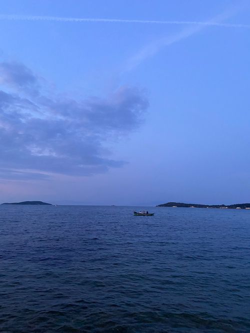 Free Serene ocean view showcasing a lone boat under evening skies in İzmir, Türkiye. Stock Photo