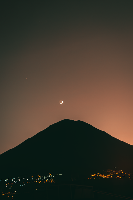 Silhouetted Misti Volcano with crescent moon over Arequipa, Peru at night, with city lights.