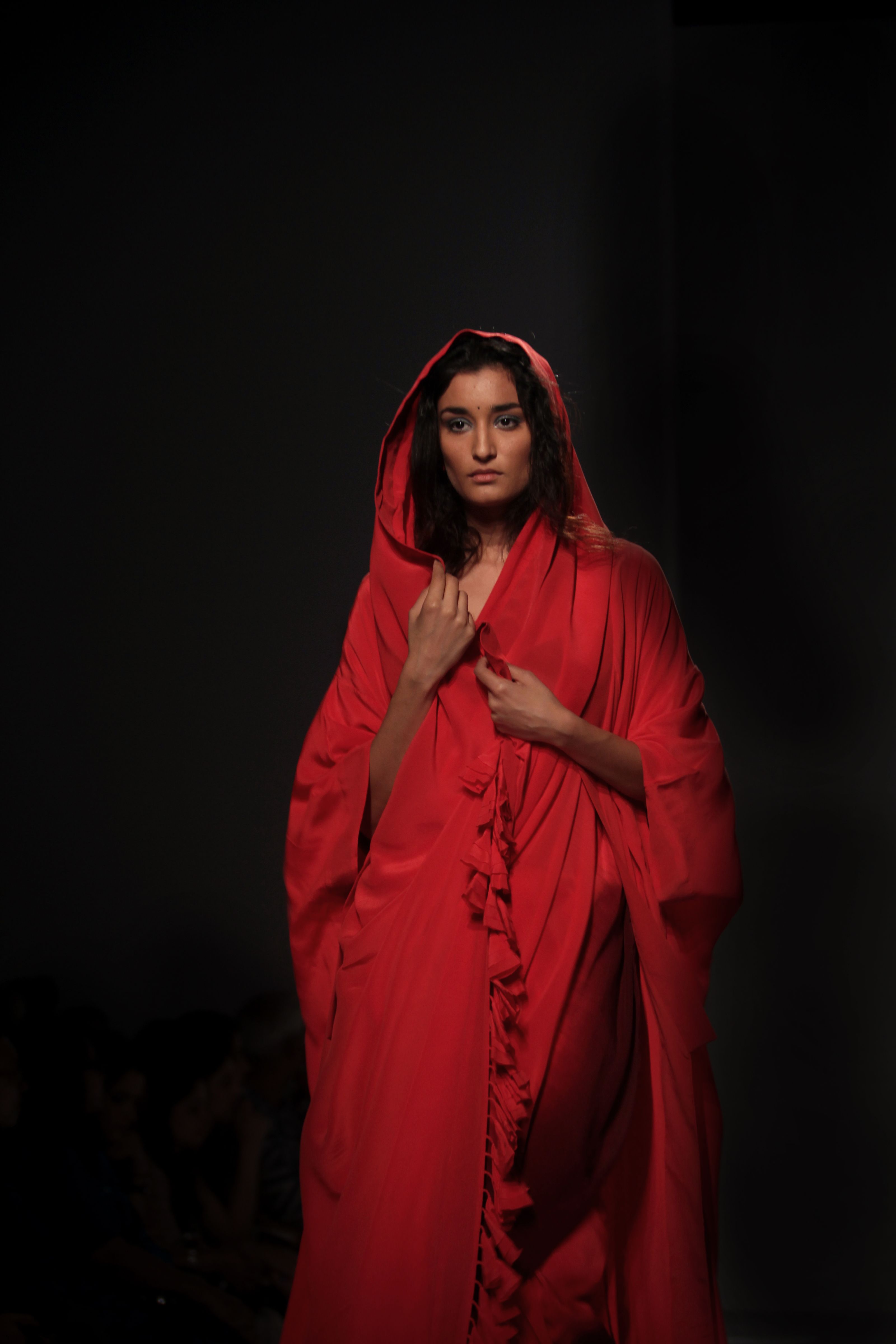 Mulher em robe vermelho caminhando confiante em uma passarela de moda. A iluminação de estúdio cria uma atmosfera dramática.