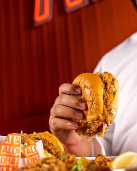 Mouthwatering close-up of a fried chicken burger being held, ideal for fast food enthusiasts.