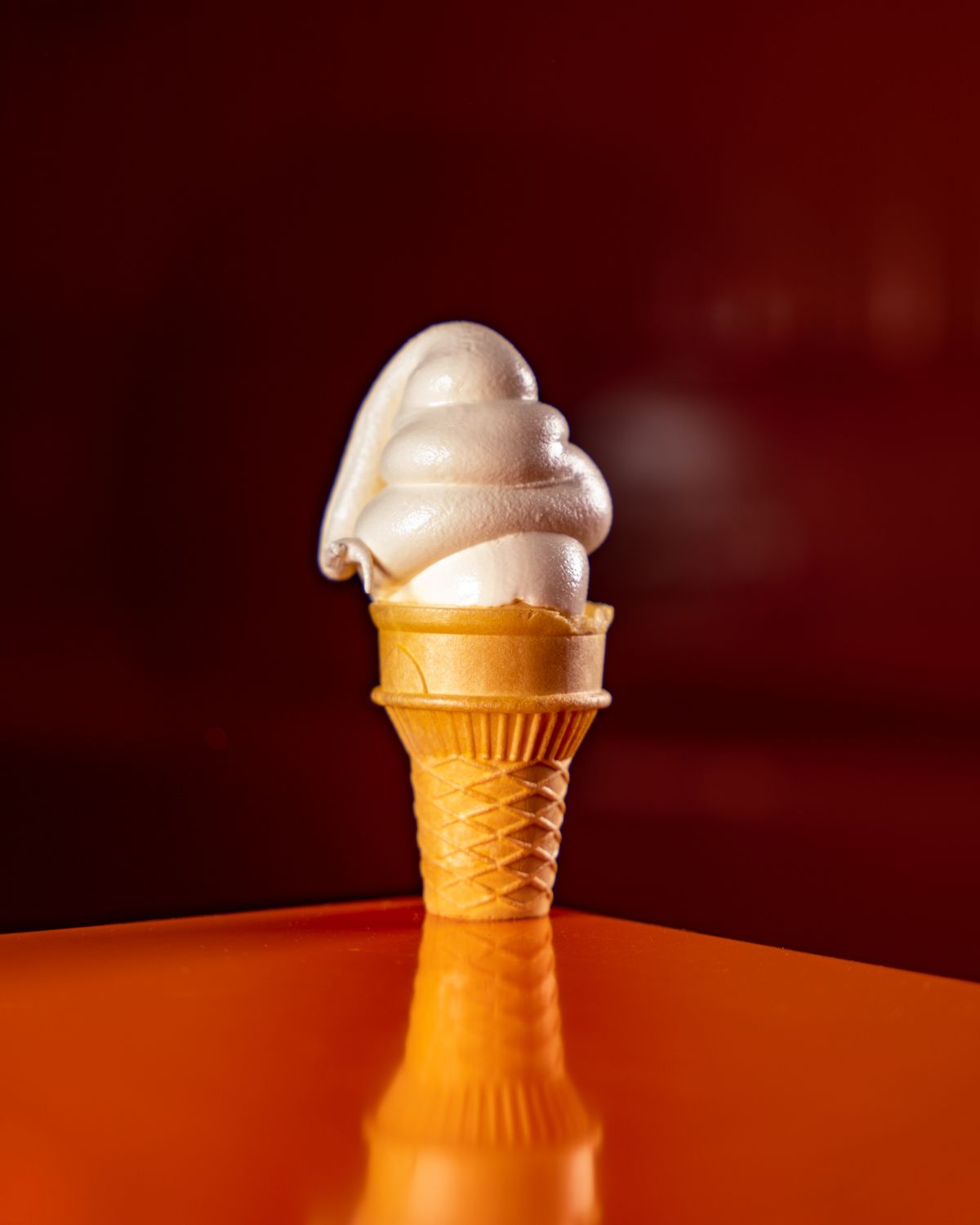 A vanilla soft serve cone standing on a plain red counter.