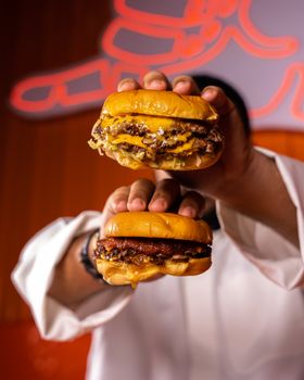 Close-up of two juicy cheeseburgers being held, showcasing melted cheese and toppings.