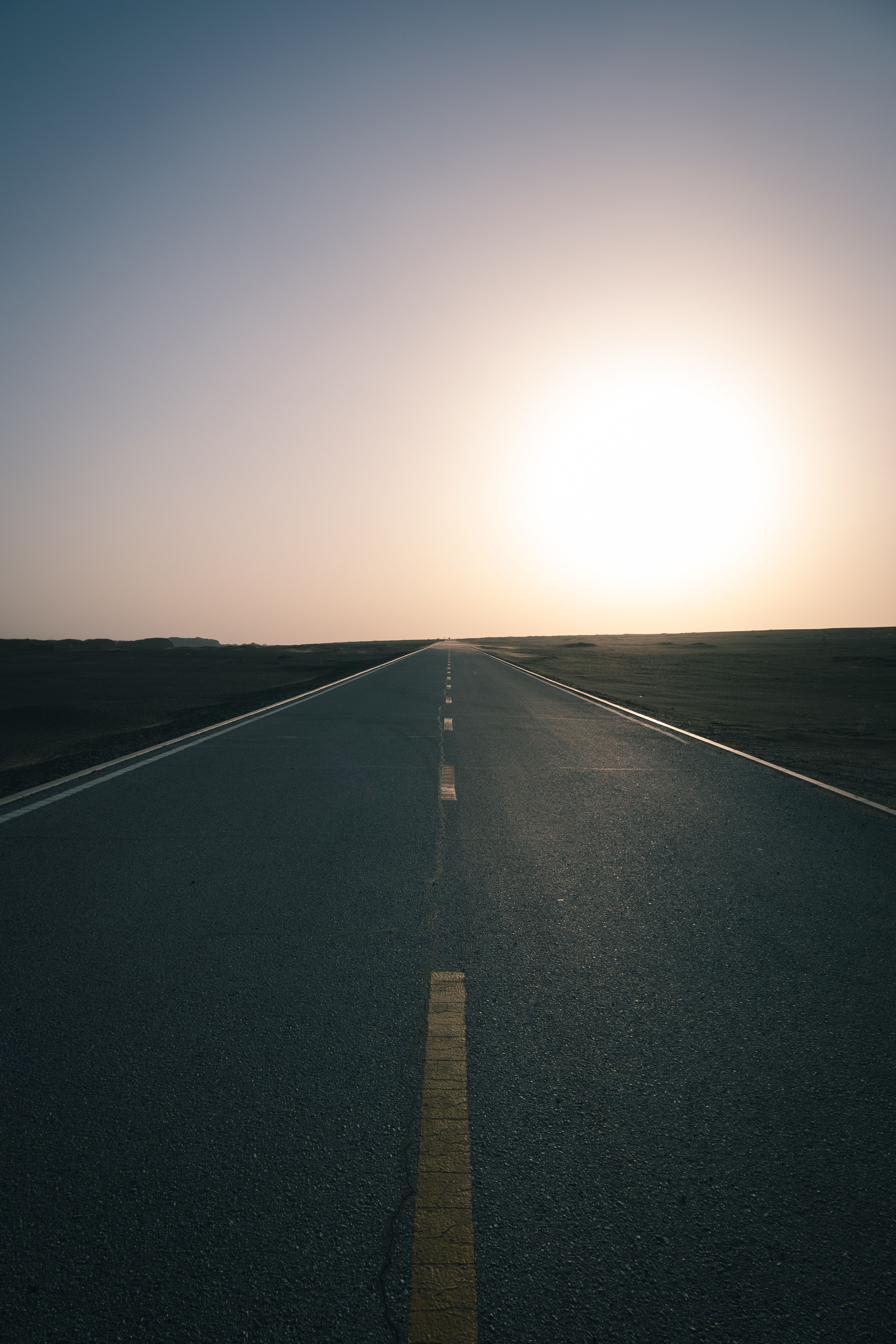 A long empty road with the sun setting in the distance · Free Stock Photo