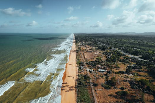 A breathtaking aerial view of a scenic beach and lush landscape meeting the ocean under a bright sky.