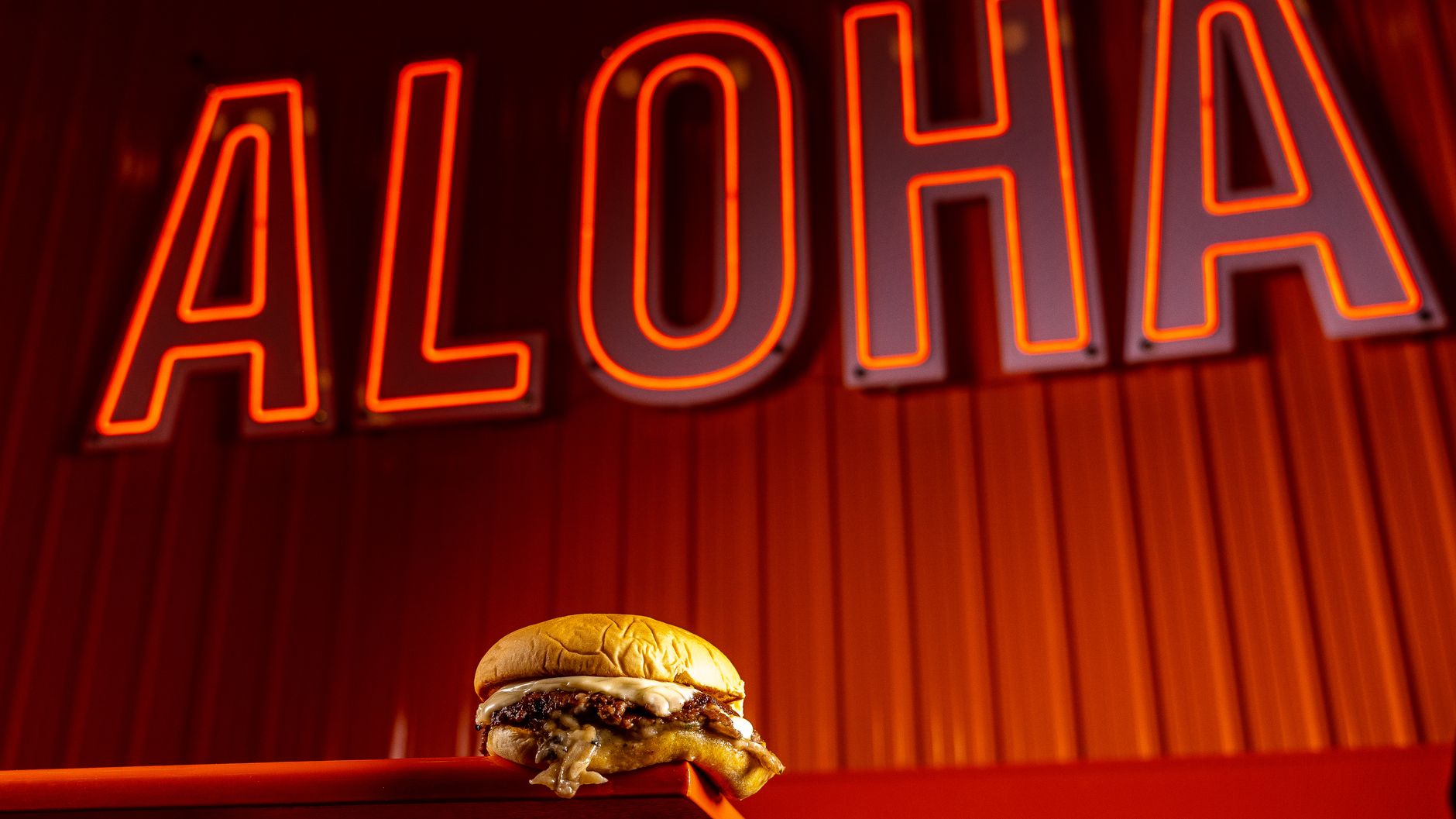 Juicy beef burger with melty cheese under a bright aloha neon sign. Perfect for food lovers.