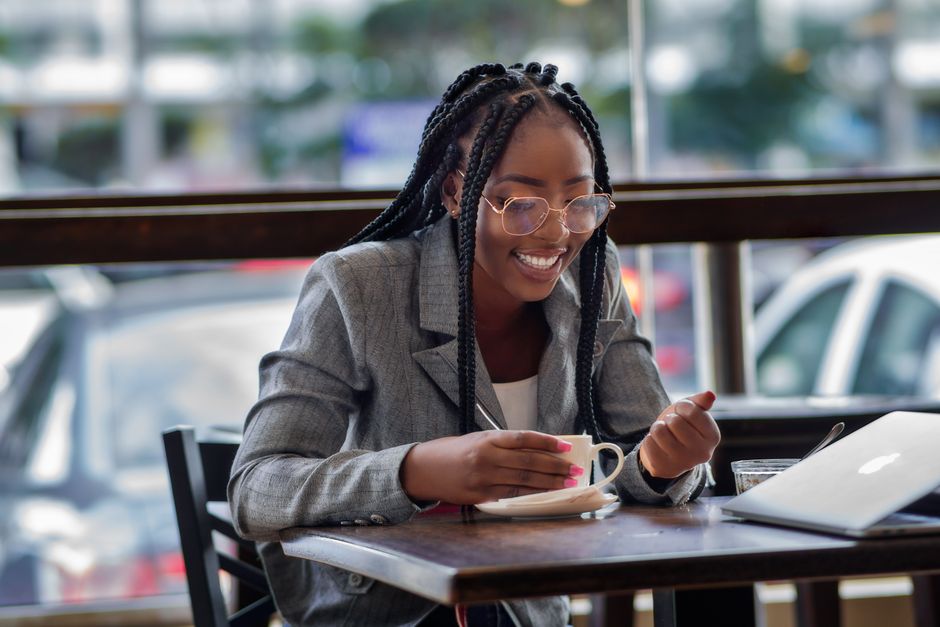 Charming African businesswoman enjoys coffee break while working at a café, embracing urban elegance.