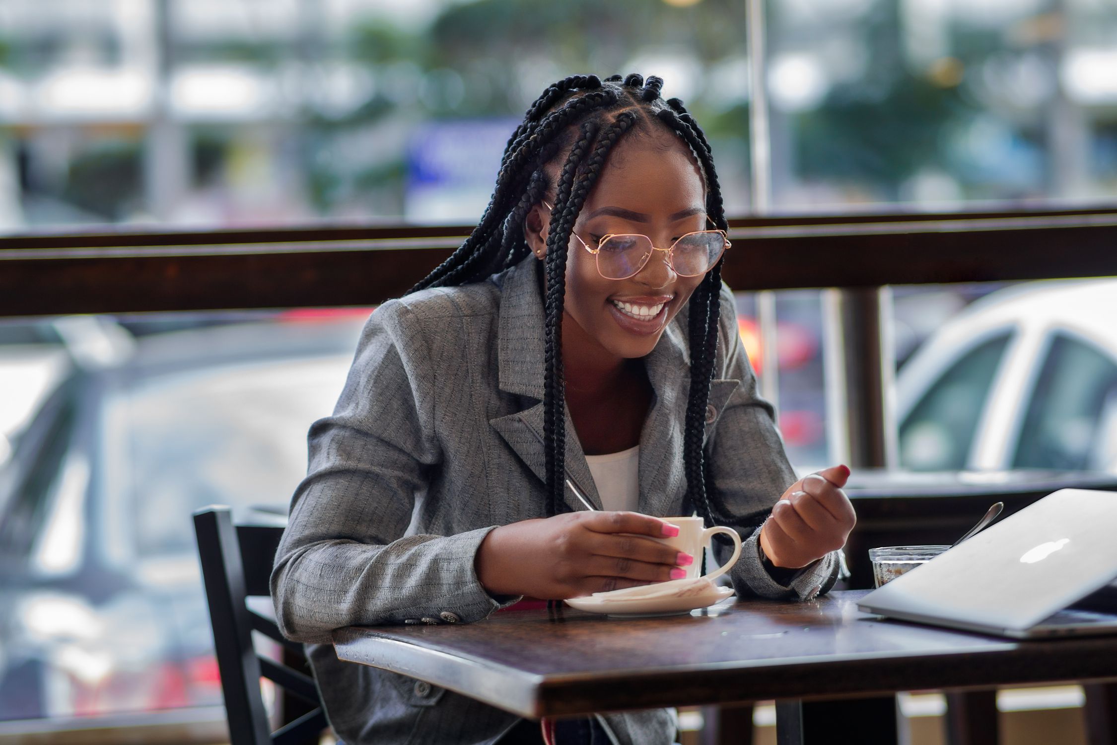 Charming African businesswoman enjoys coffee break while working at a café, embracing urban elegance.