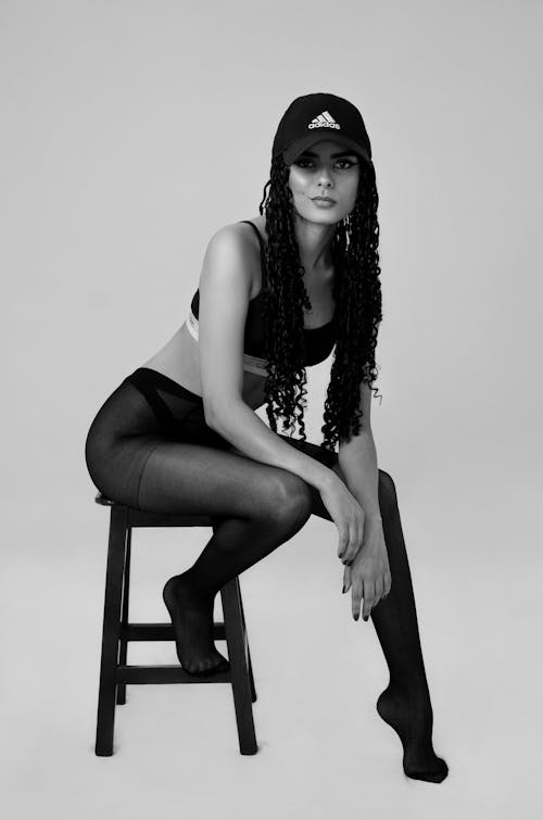 Black and White Shot of a Young Brunette Woman in Opaque Tights Sitting on a Stool