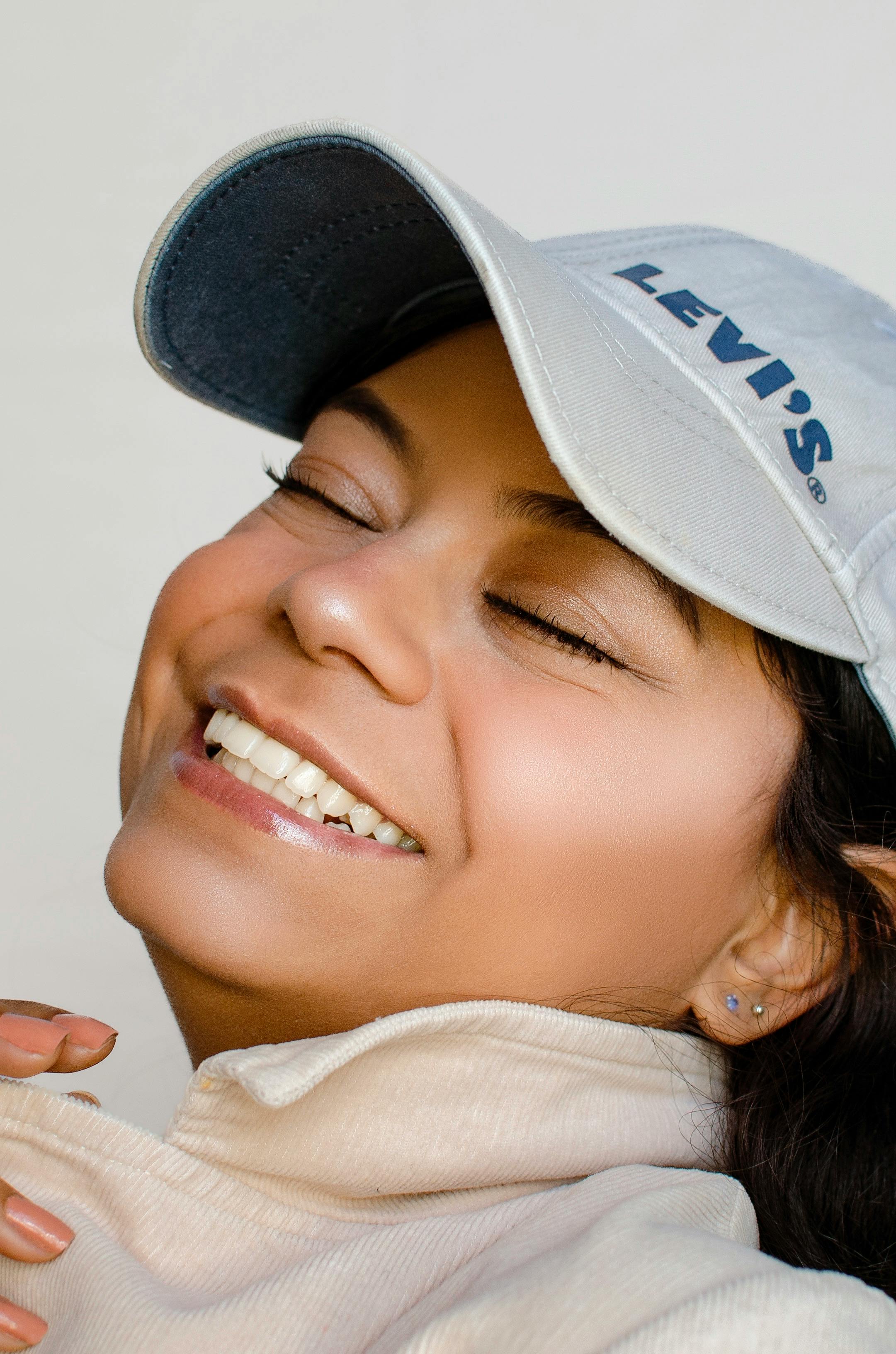 A joyful woman wearing a blue baseball cap smiles with eyes closed, capturing a moment of happiness.