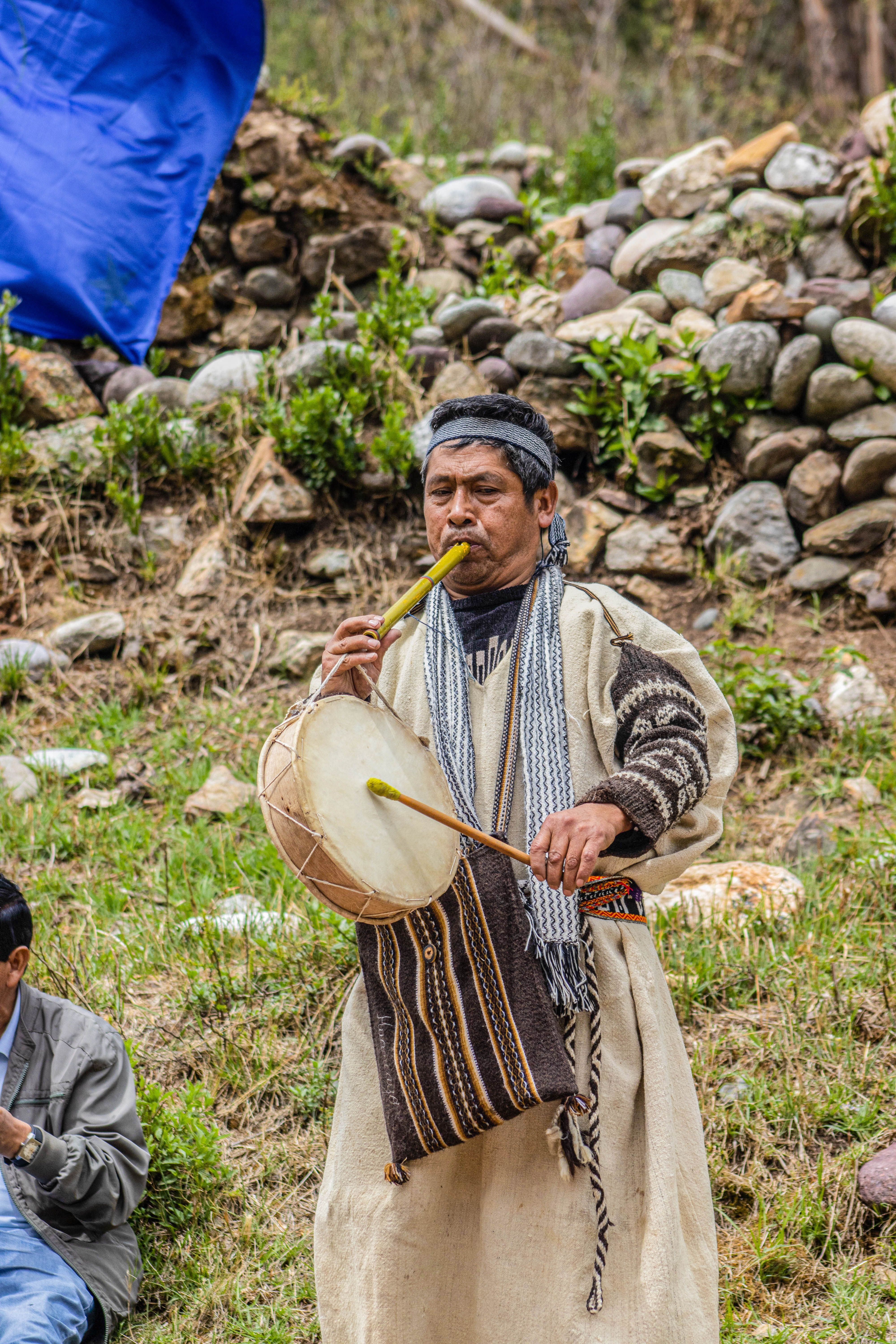 A musician in traditional attire plays flute and drum in Concepción, Peru's scenic outdoors.
