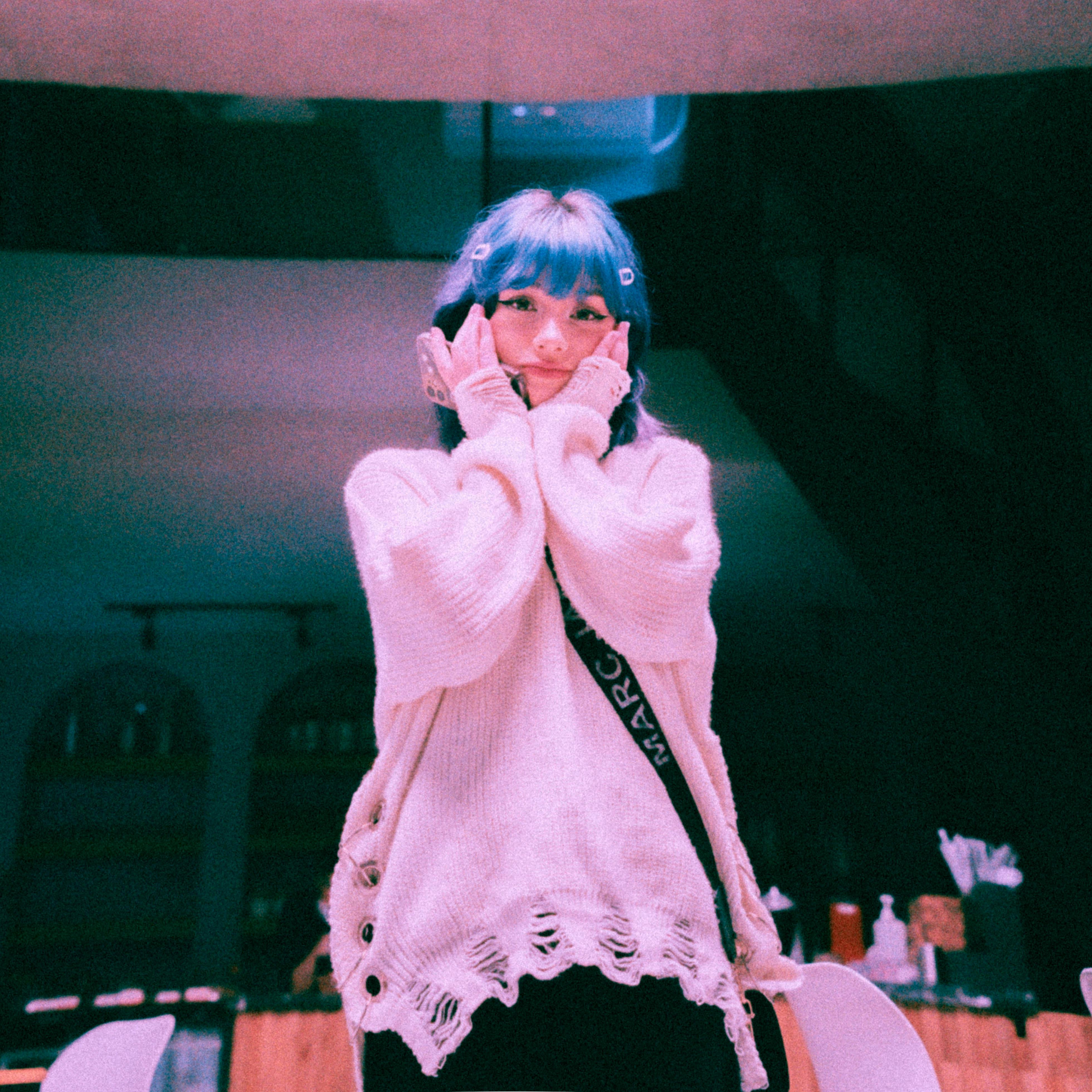 Young woman with blue hair and cozy sweater posing in a stylish indoor setting.