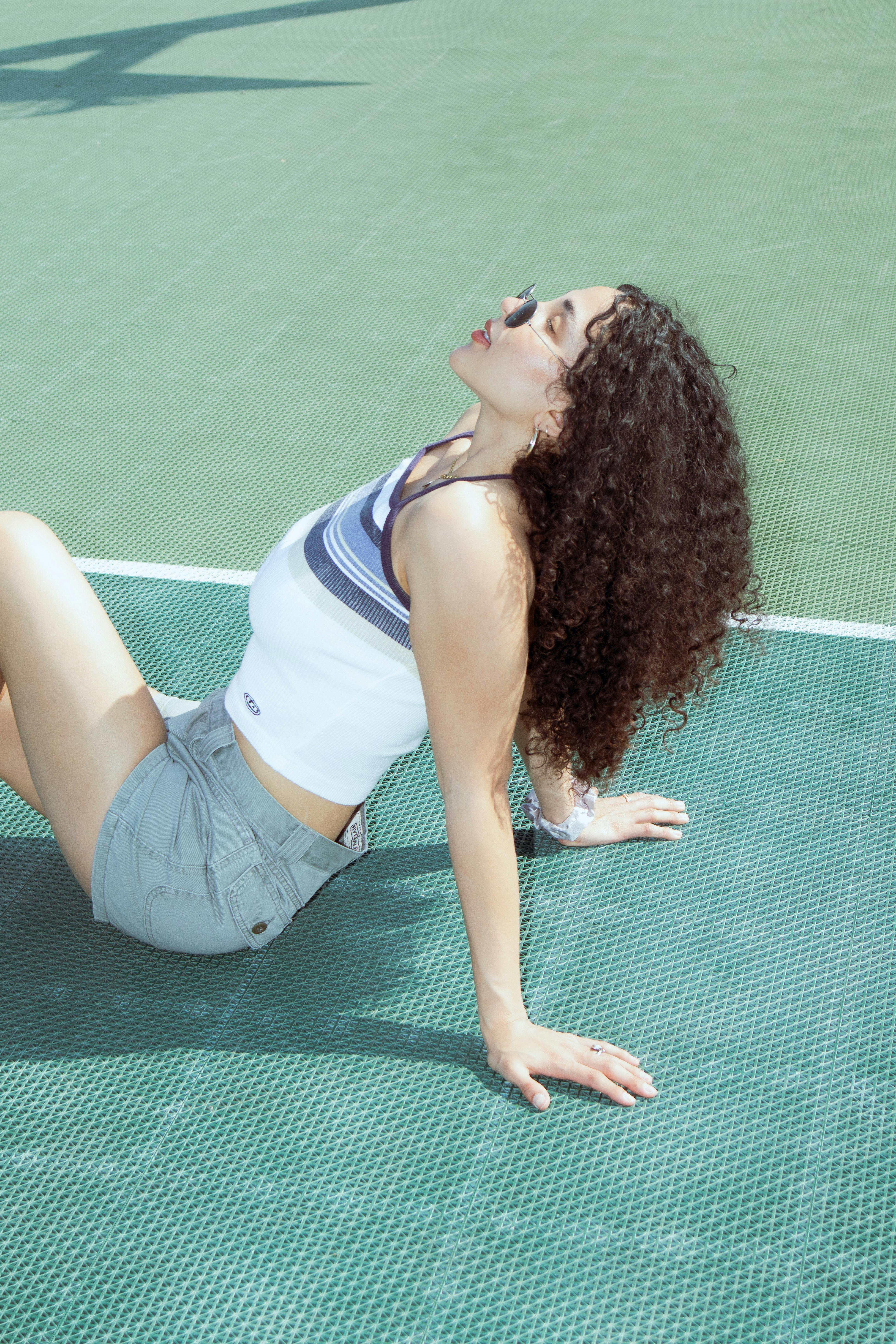 Relaxed young woman with curly hair enjoying the sun on a tennis court.